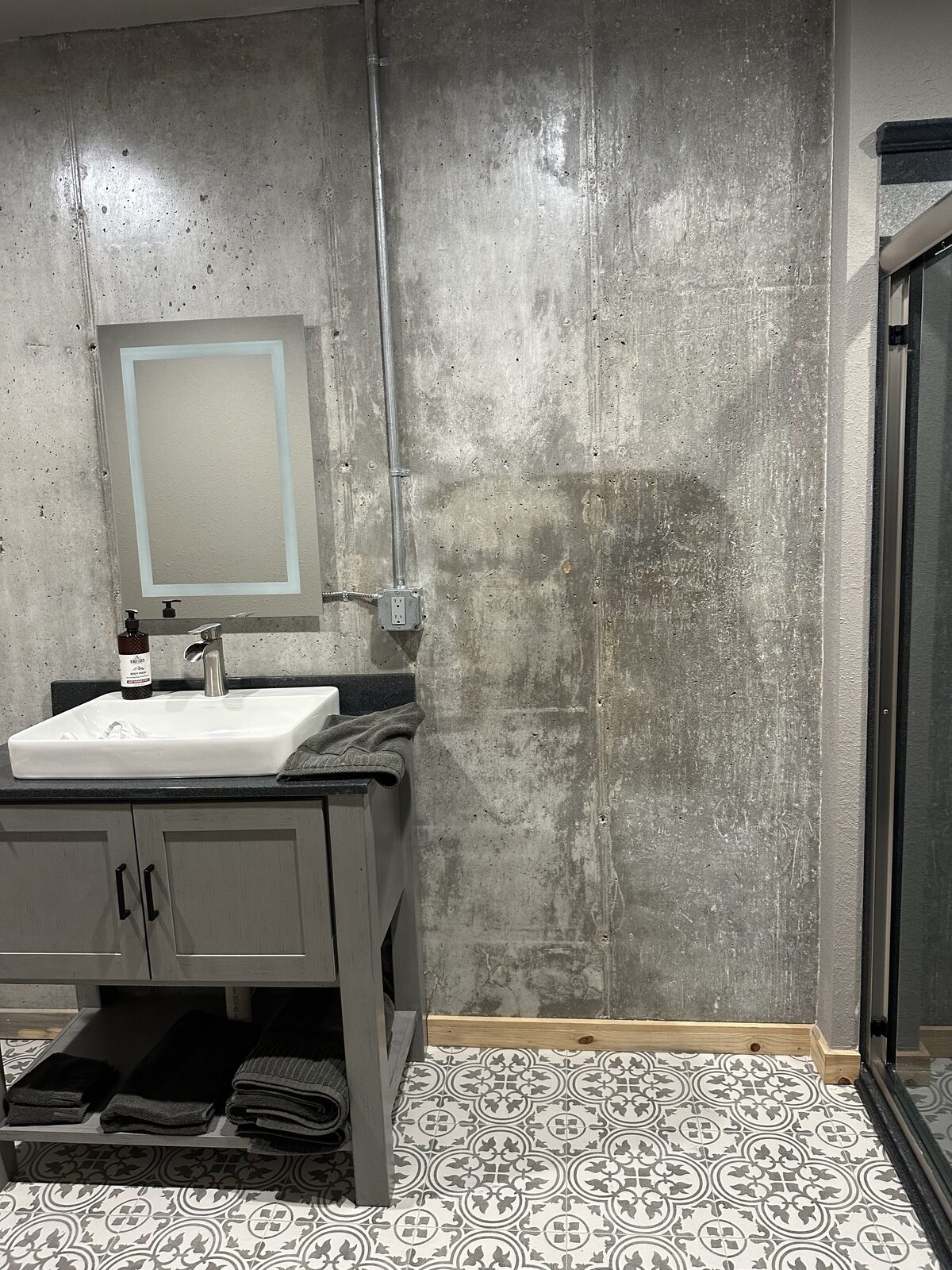 Industrial barndominium bathroom with polished concrete wall, vessel sink vanity, and patterned tile floor in Oklahoma