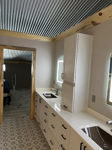 Barndominium bathroom with double vanity, lighted mirrors, and corrugated metal ceiling in Oklahoma