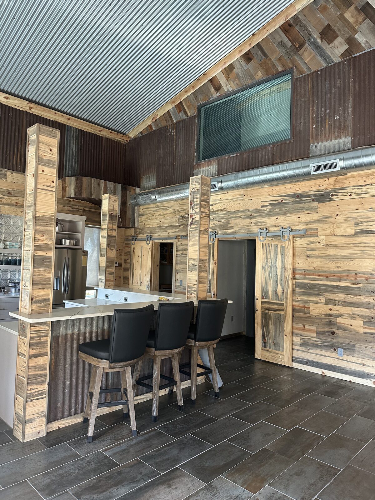 Barndominium kitchen and breakfast bar with sliding barn doors and corrugated metal accents in Oklahoma