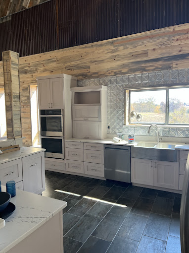 Barndominium kitchen with white cabinets, pressed tin backsplash, and reclaimed wood beam in Oklahoma