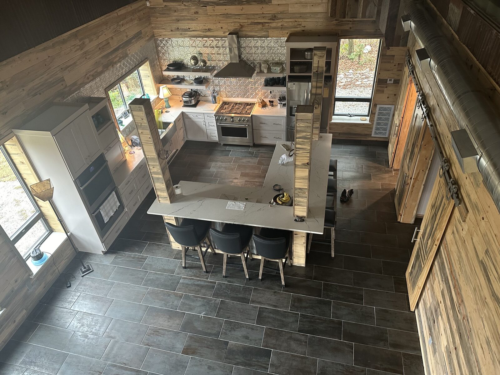 Loft view of an open barndominium kitchen with quartz island, tin backsplash, and tile floors near Seminole, OK